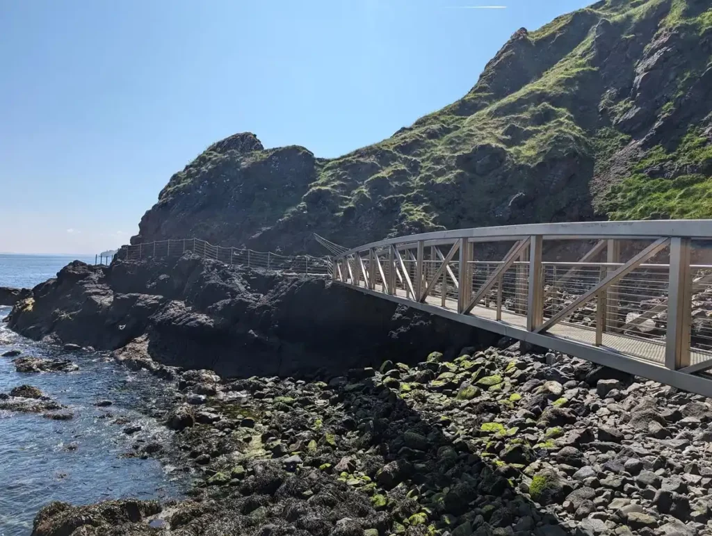 A metal bridge over a small bay at the base of a rocky cliff