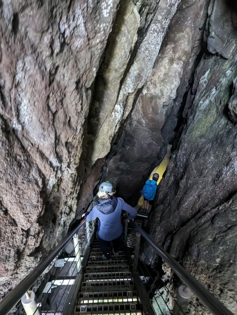 People descending metal steps into a narrow underground ravine.