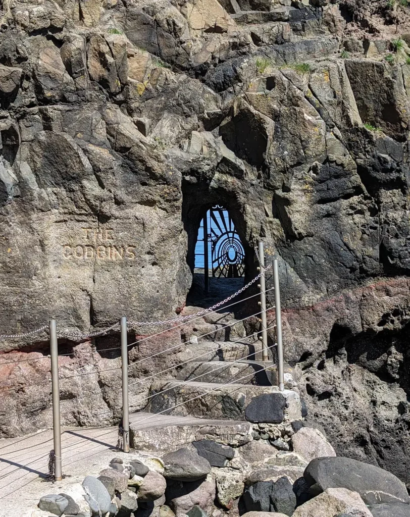 A rock cliff with steps leading up to a small opening, just big enough for a person to crouch down to enter.