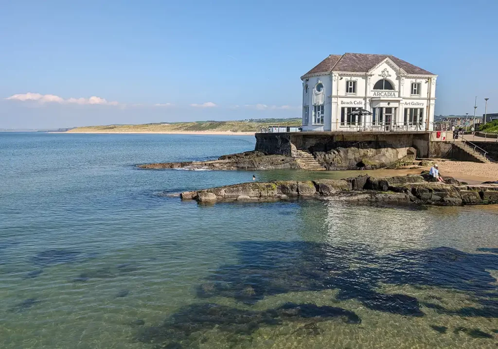 A white building named Arcadia with a cafe and gallery inside, jutting out into the sea with a shallow bay in front