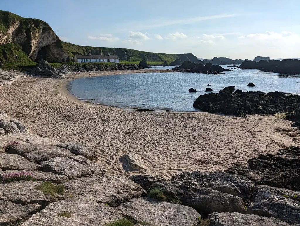 A small sandy beach in a rocky bay. There are some small white cottages on the other side of the bay.