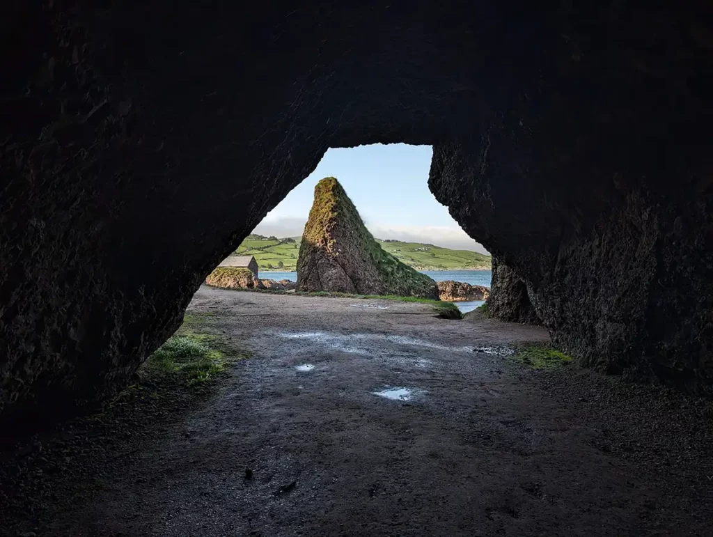 Looking out to a rocky beach from inside a large dark cave