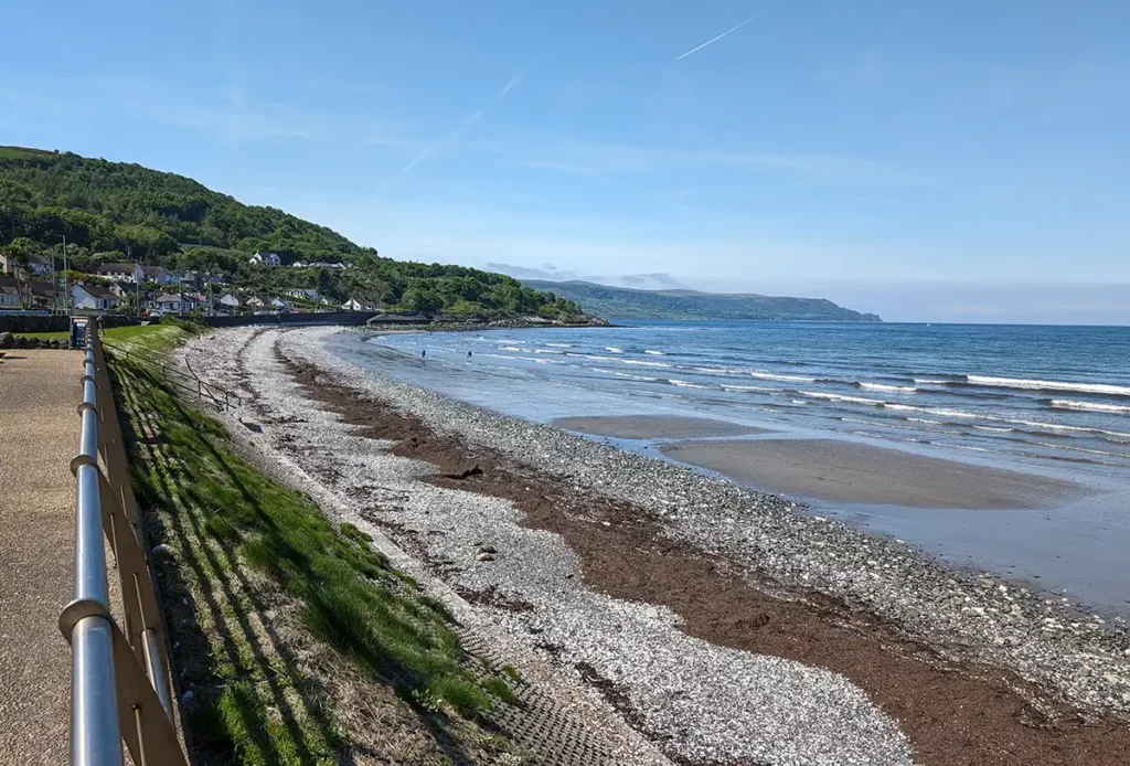 A pebble and sand beach at the seaside, with green hills behind