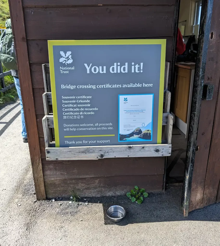 A National Trust sign reading 'You did it!' and encouraging visitors to pick up a certificate to show they've crossed the bridge