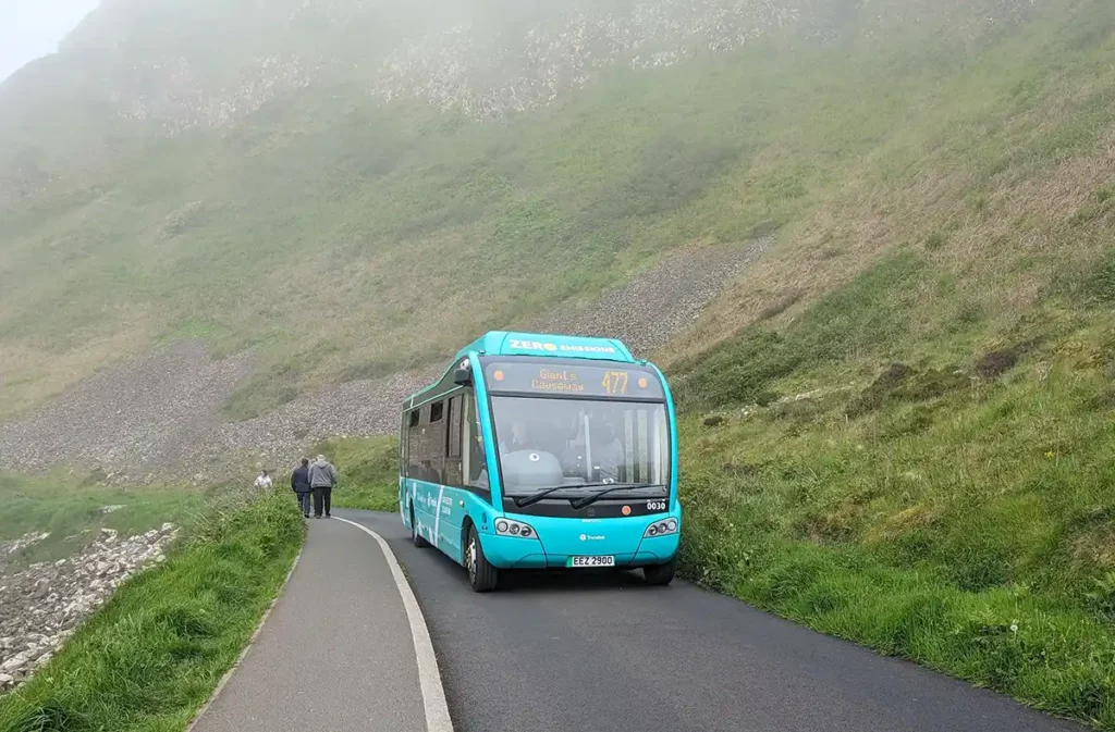 A bright green bus driving along the road back up to the visitor centre