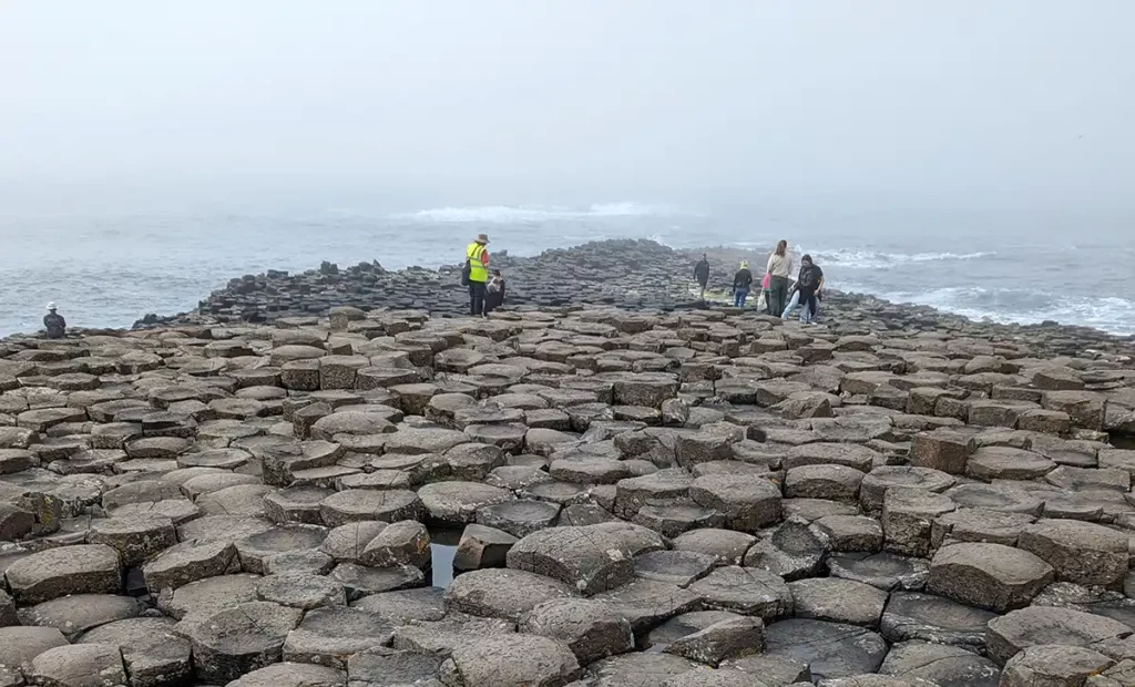 The stones stretching into the sea. There are some people clambering on the rocks.