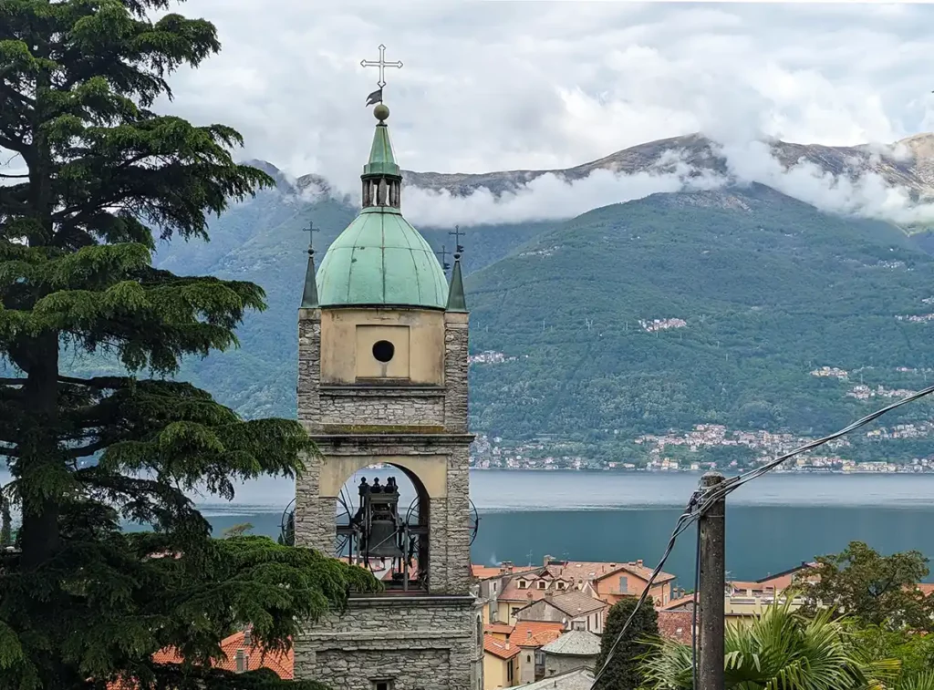 A church tower in a lakeside village. The image shows the lake and mountains beyond. 