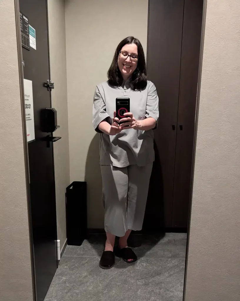 A woman wearing grey, Japanese-style pyjamas taking a photo in the mirror