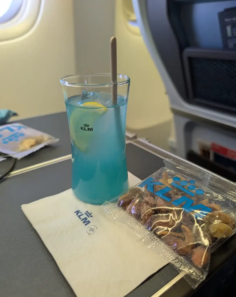 A blue drink and some nuts on a plane's tray table