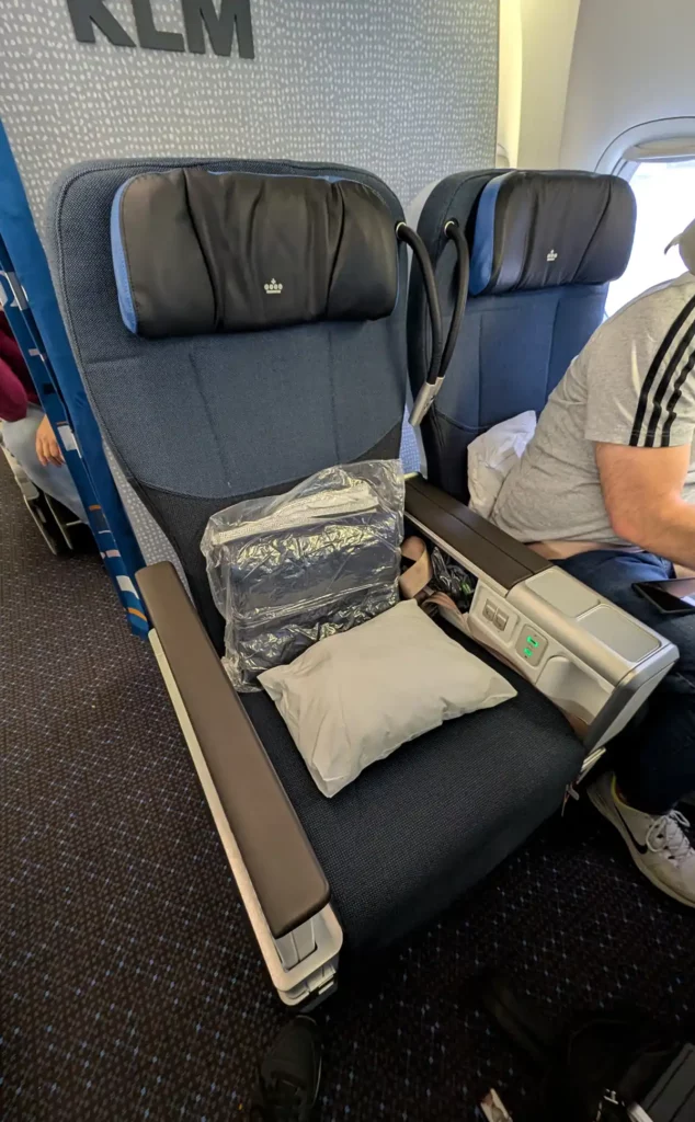 A KLM premium economy seat on a Boeing 777. The seat is larger than an economy plane seat. There's a pillow and blanket on the seat.