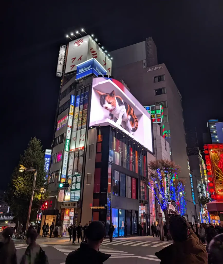 An electronic billboard with a 3D cat at the top of modern buildings in Tokyo