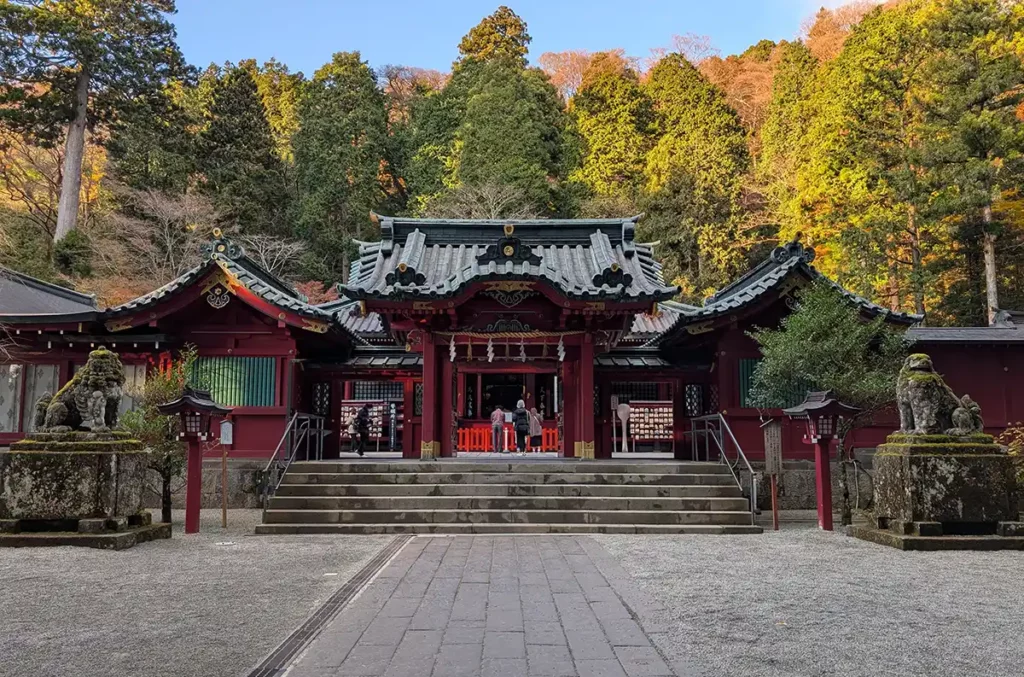 A Shinto shrine with dark wood and red accents, set deep in some woods