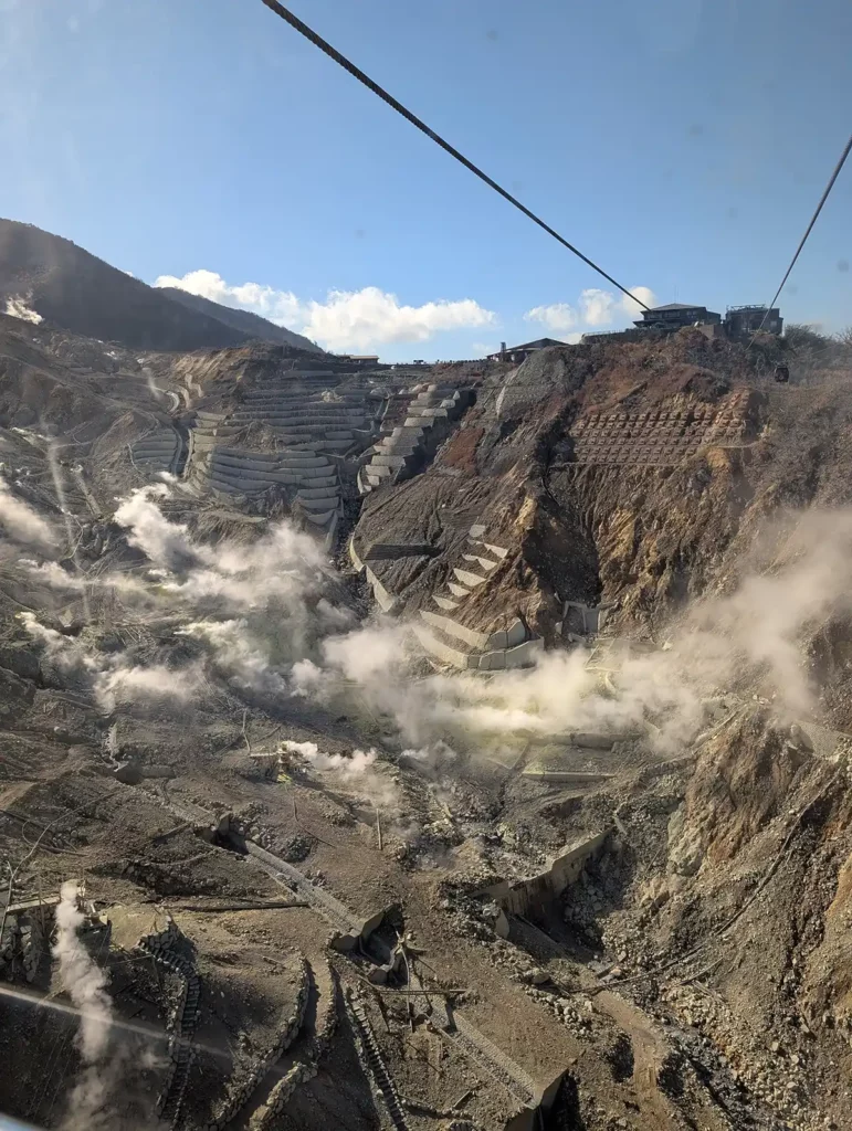 A shot taken from the Hakone Ropeway cable car. The cable car is high in the air over a rocky valley, with multiple steaming sulphur vents.