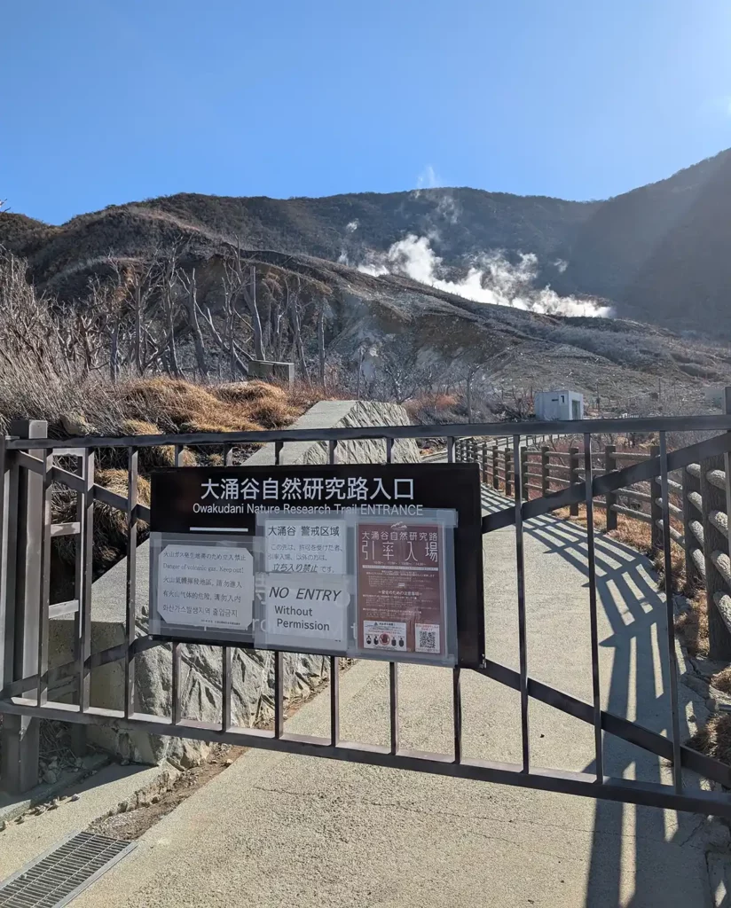 Steaming sulphur vents rising from a mountain. There's a path, but the gate is closed and a sign says that entry is forbidden. 