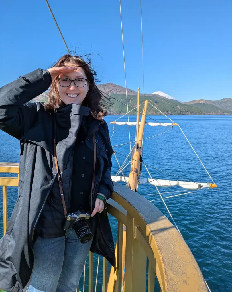 A woman standing on the deck of a pirate ship cruise. Her hair is blowing all over the place and she's smiling and squinting into the sun. 