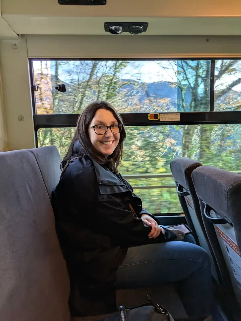 A woman sat on a bus, with trees outside the window