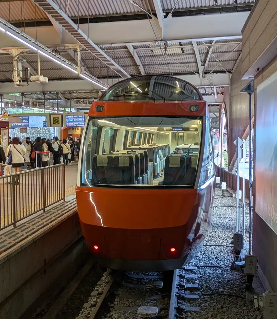 A red Romancecar train at a station platform