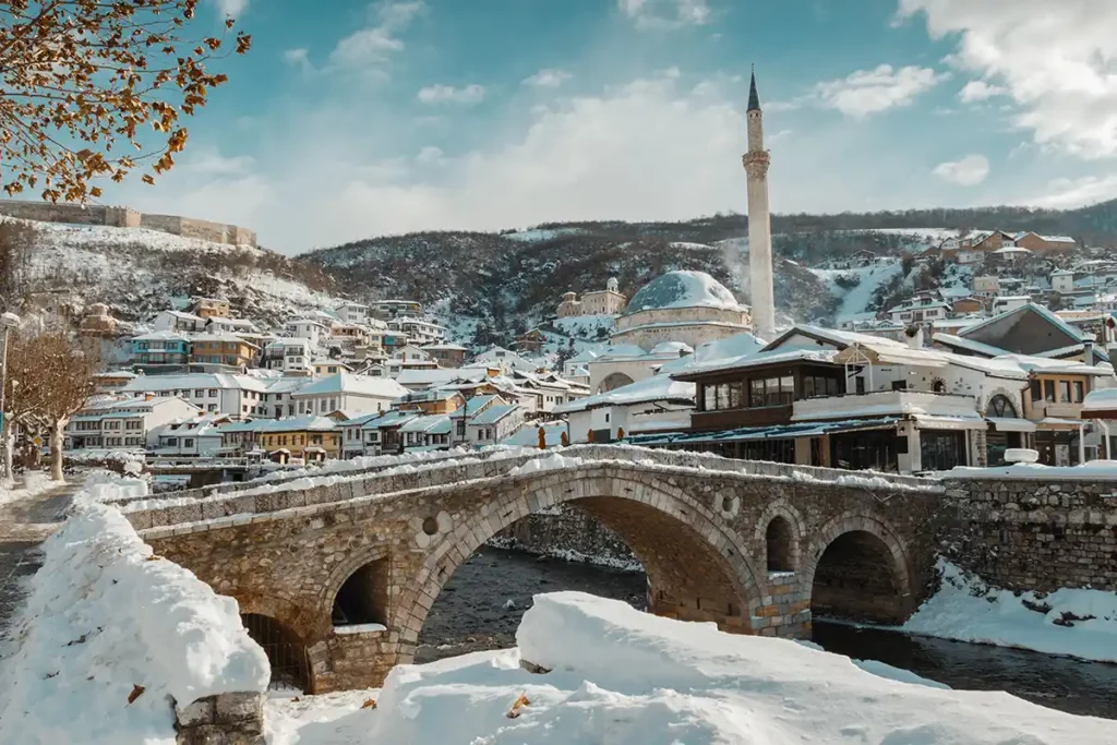 An old stone bridge over a river, covered in snow