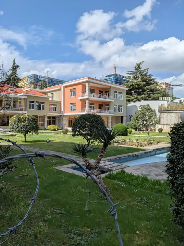 A 3-storey, modernist house in a large garden, behind barbed wire