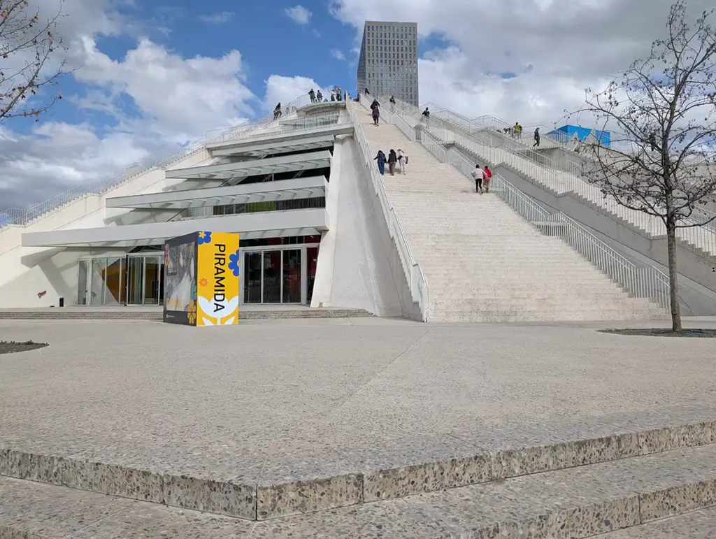 A large white pyramid-shaped building, with people climbing the steps to the top